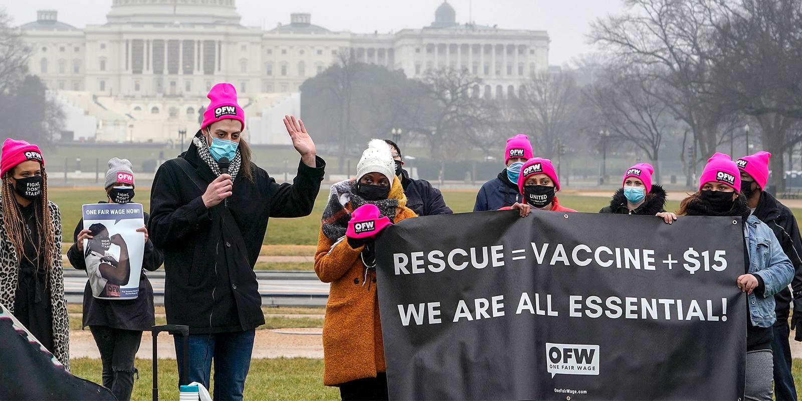 Protestors holding banner that says "RESCUE = VACCINE + $15", next line "WE ARE ALL ESSENTIAL"